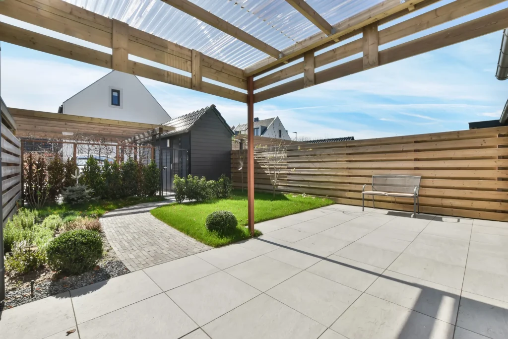 Modern backyard patio featuring large concrete pavers, a wooden pergola, and a landscaped walkway leading to a garden shed.
